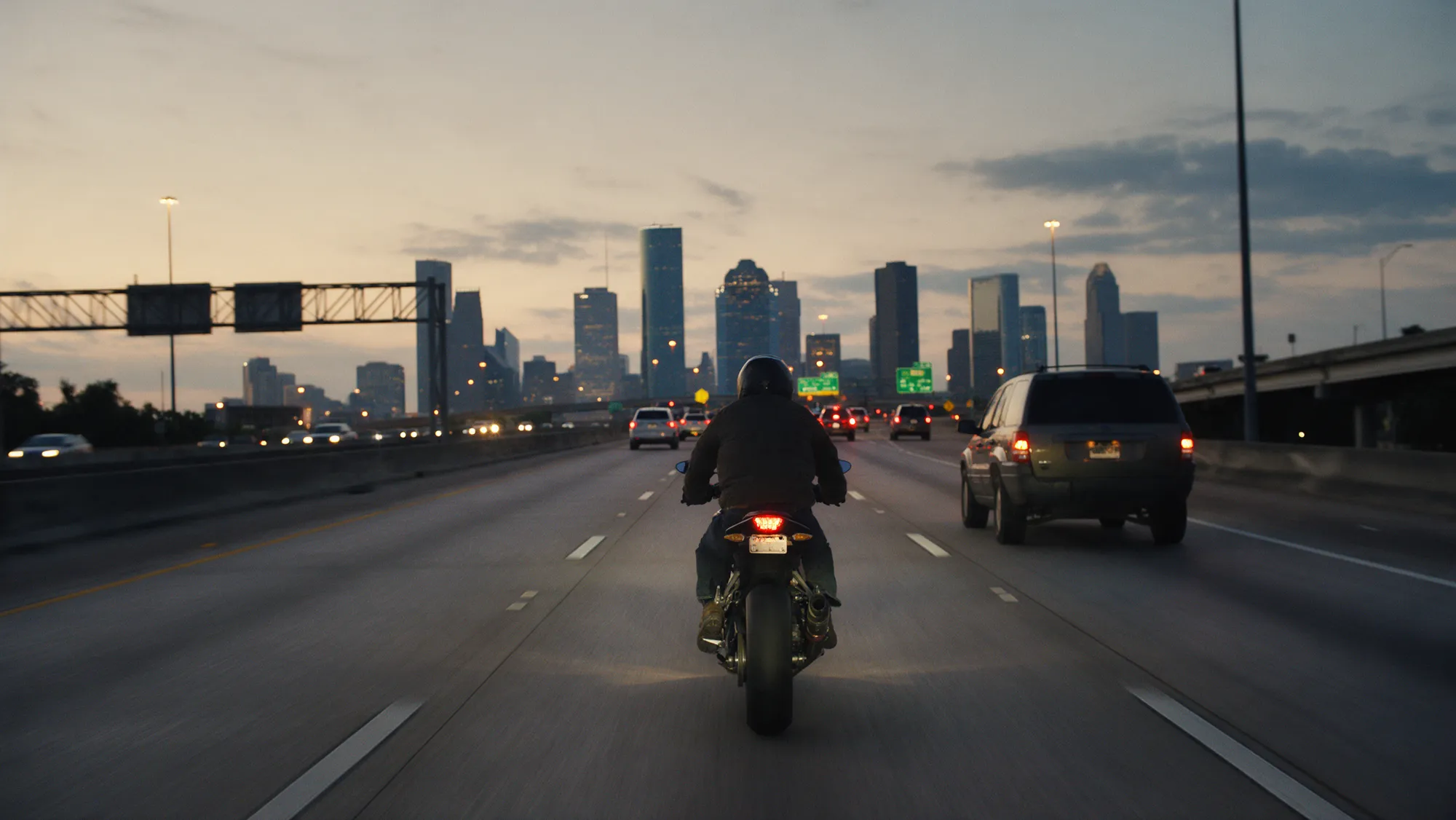 A motorcyclist seen from behind riding in the center of a Houston freeway lane at dusk