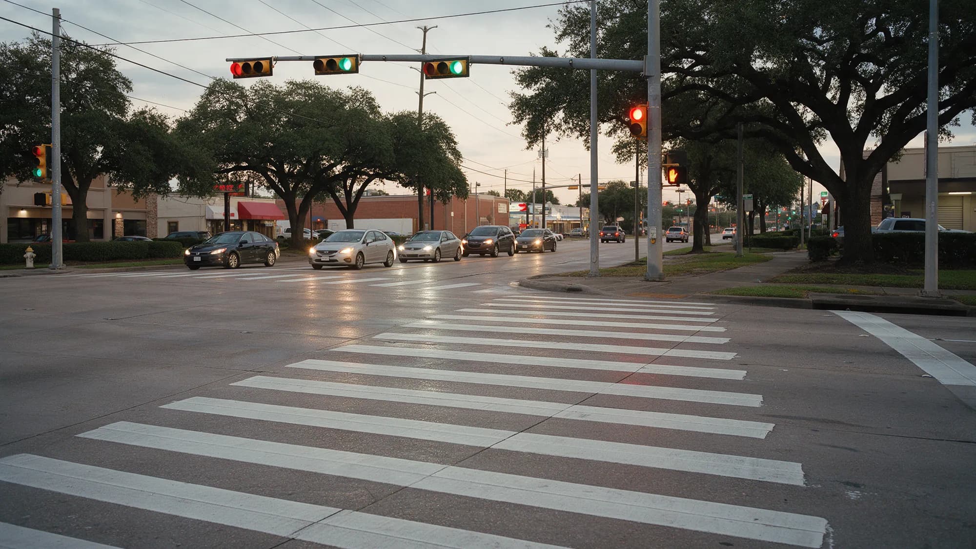 An empty marked crosswalk at a Houston intersection at dusk with cars waiting at the stop line