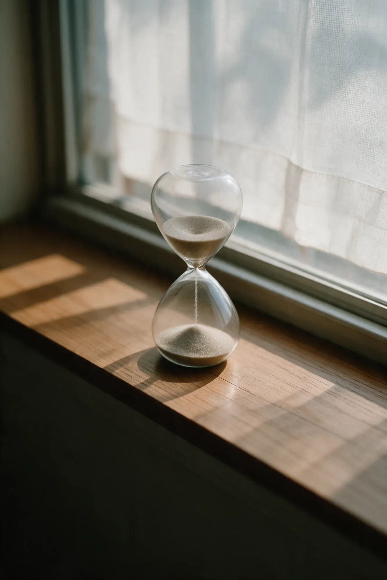 An hourglass with sand running on a sunlit windowsill